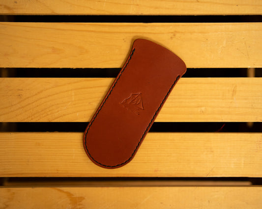 Brown leather skillet handle cover with a logo on a wooden surface
