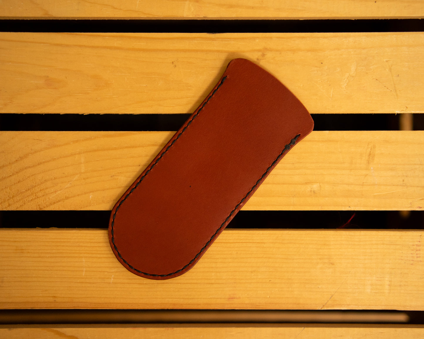 Brown leather skillet handle cover with a logo on a wooden surface