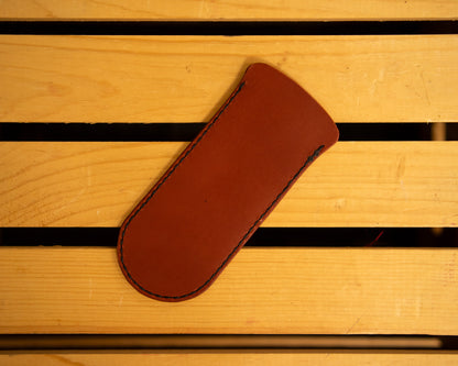 Brown leather skillet handle cover with a logo on a wooden surface